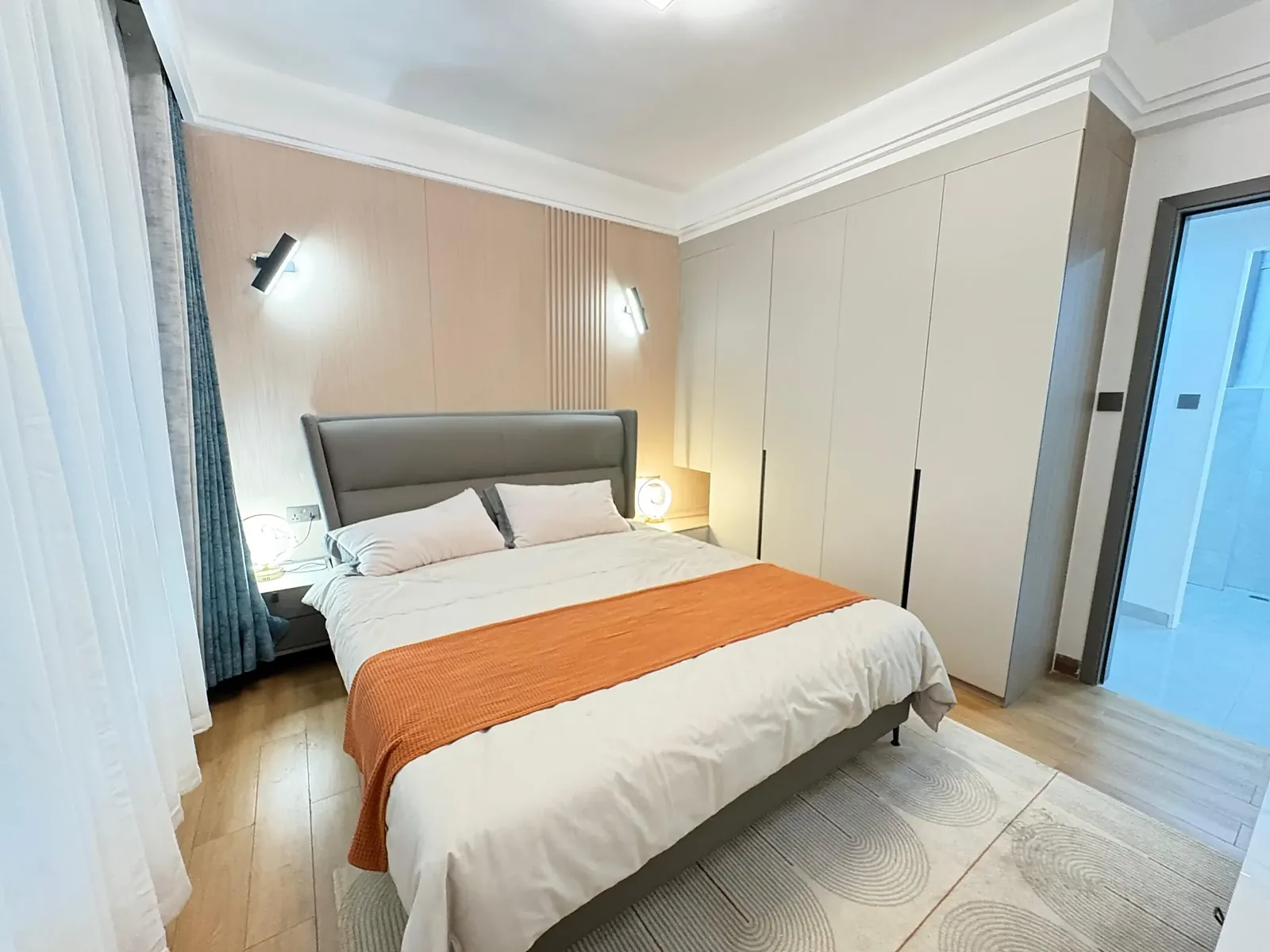 Bedroom at Capital Garden, Hurlingham, with a grey upholstered bed, orange throw and tall white wardrobes.