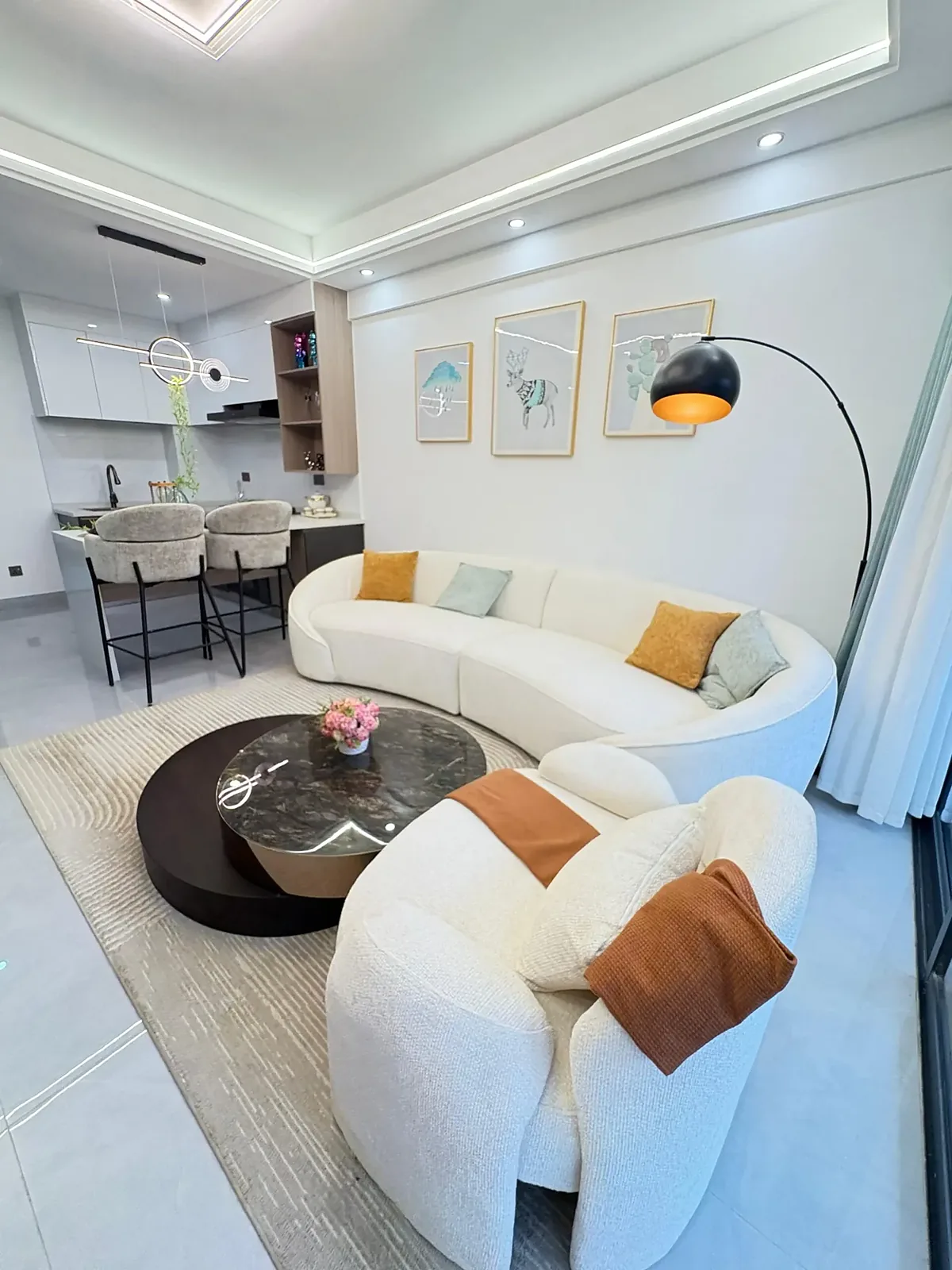 Living area at Capital Garden, Hurlingham, with a curved cream sofa, round coffee tables and open kitchen.