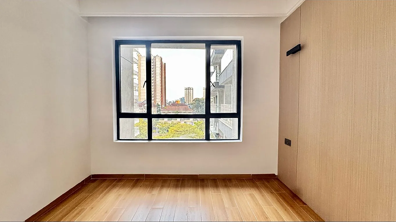 Unfurnished room at Capital Garden, Hurlingham, with a large black-framed window, wood-look flooring and textured accent wall.