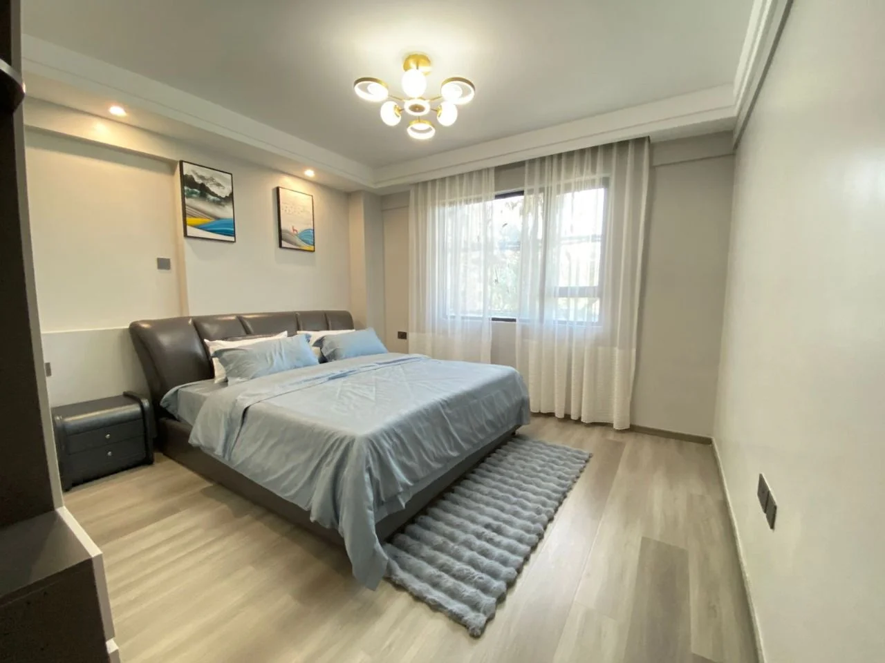 Bedroom at Golden Street Residency, Kileleshwa, with blue bedding, a padded headboard and sheer window curtains.