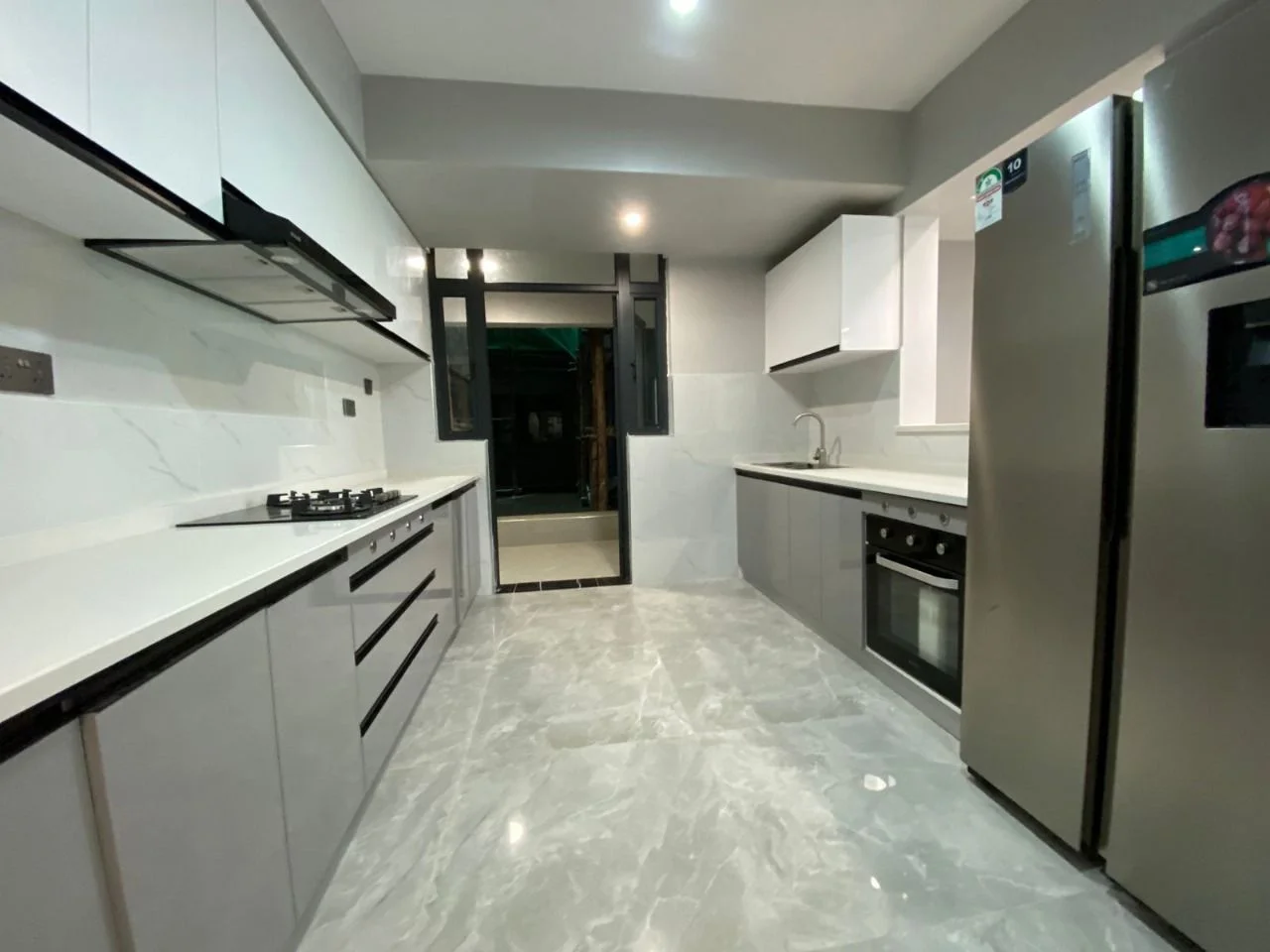 Galley kitchen at Golden Street Residency, Kileleshwa, with white and grey cabinets, gas hob, oven and refrigerator.