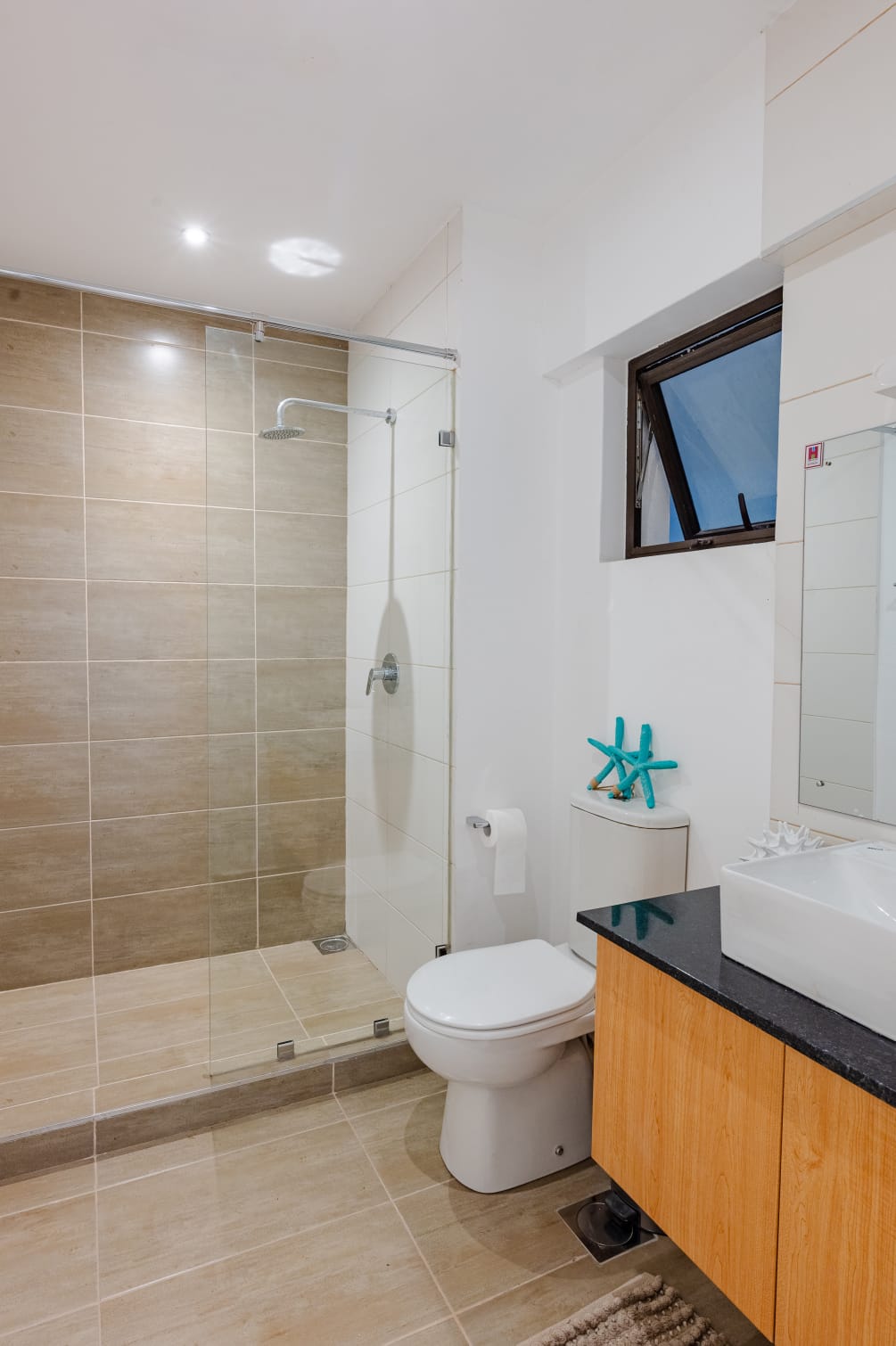 Bathroom in a Kilimani apartment with a glass-enclosed shower, beige tiles, toilet and wood-finish vanity.