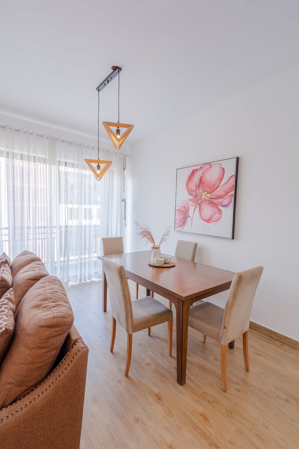 Kilimani apartment dining area with a wooden table, four upholstered chairs, triangular pendant lights and floral artwork.