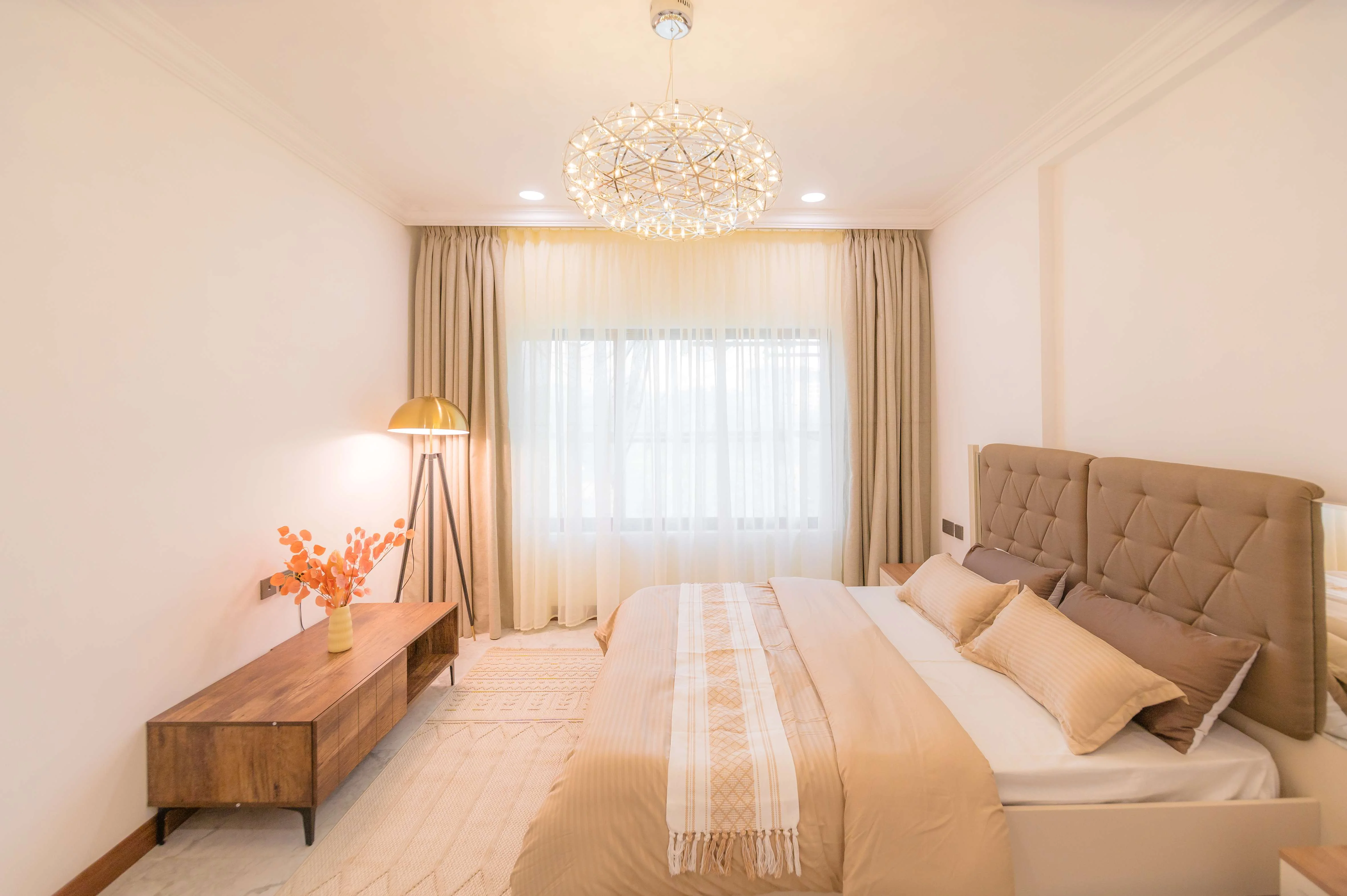 Bedroom at Kings Pinnacle, Westlands, with a tufted headboard, beige bedding, chandelier and large curtained window.