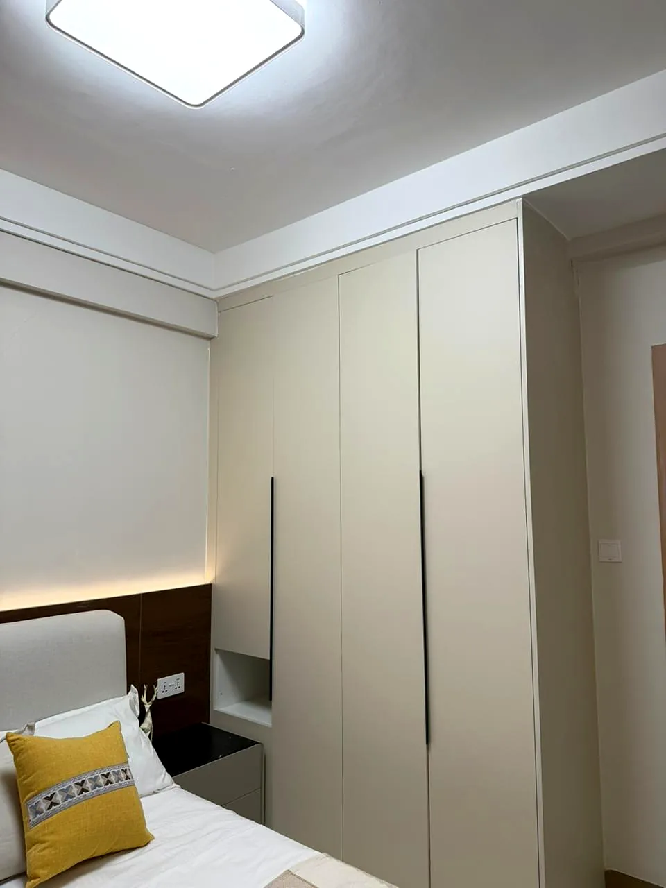 Cream fitted wardrobes with black handles beside a bed with a yellow cushion at Lido Garden, Kilimani.