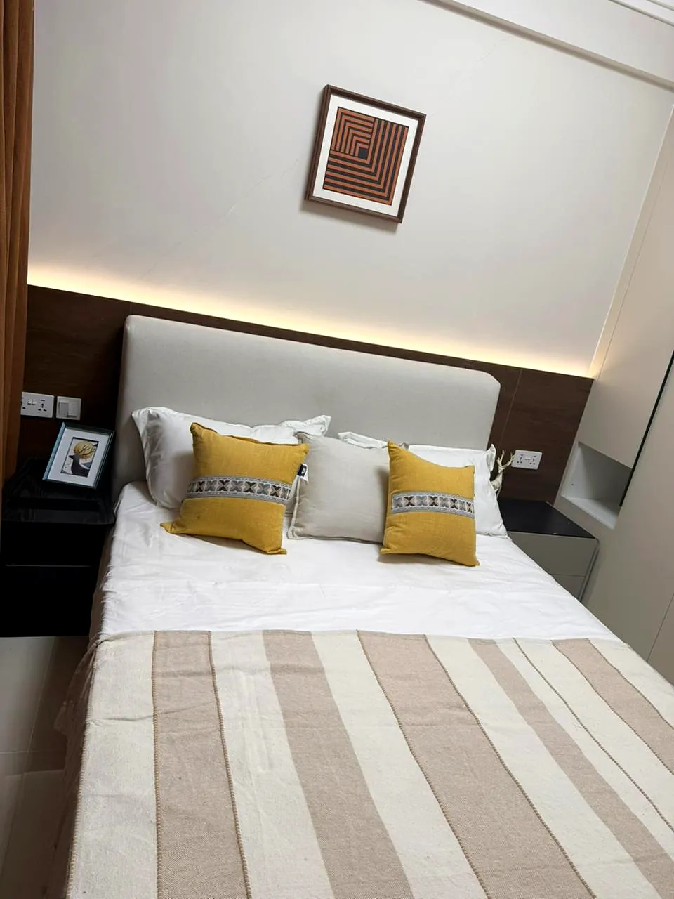 Bedroom at Lido Garden, Kilimani, with an upholstered headboard, yellow cushions and a striped bed throw.