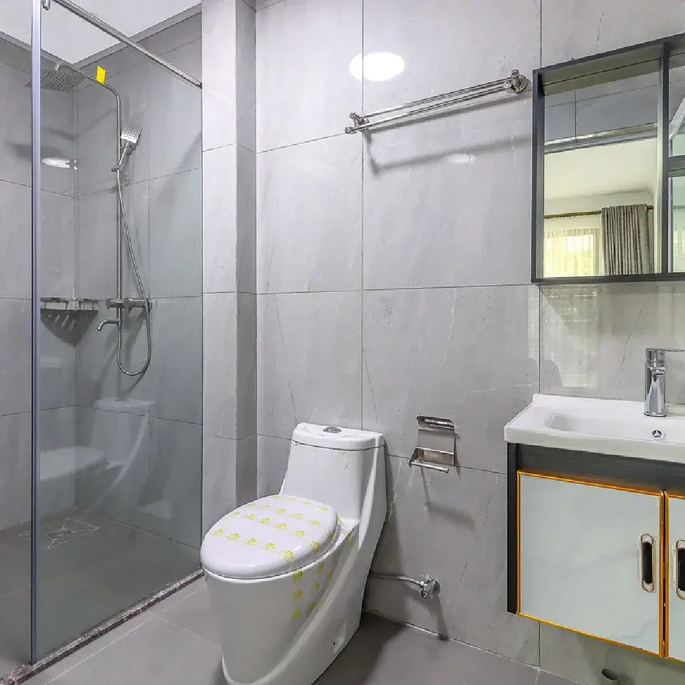 Marigold II Langata bathroom with grey tiles, glass-enclosed shower, toilet, vanity sink and mirror.