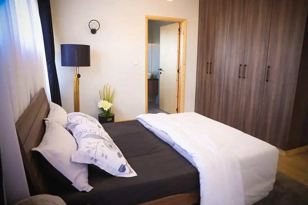 Bedroom at Marigold II Langata with white bedding, tall wardrobes and a black-shaded floor lamp.