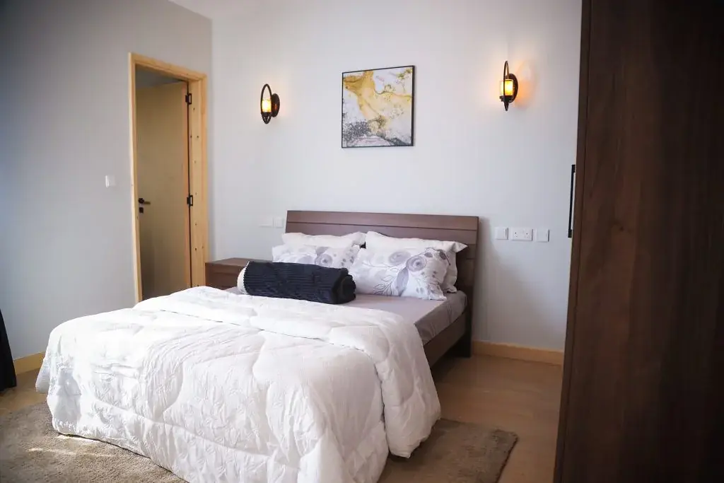 Bedroom at Marigold II Langata with white bedding, a dark headboard and two illuminated wall sconces.