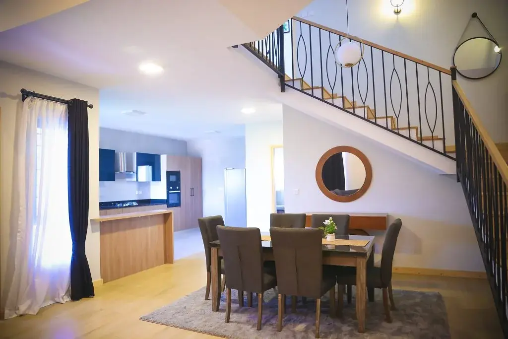 Dining area with upholstered chairs, an adjoining kitchen and staircase at Marigold II Residency in Langata.