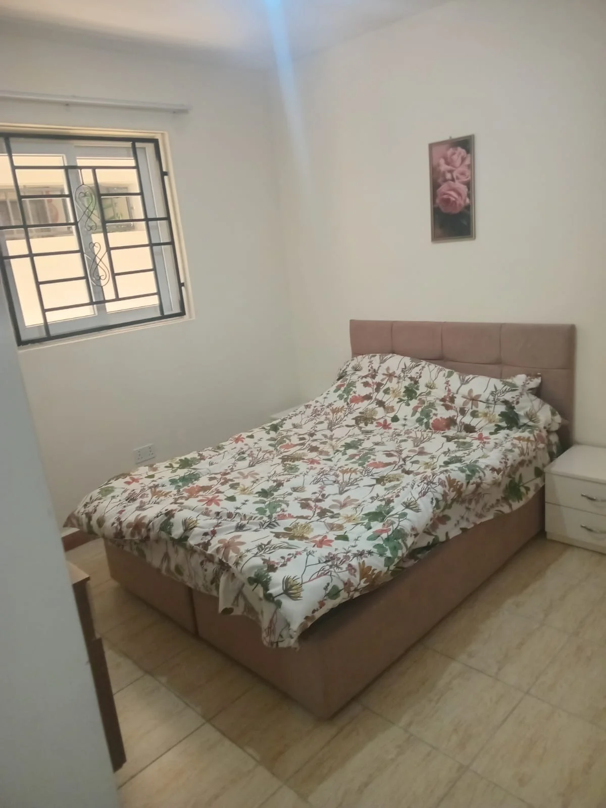 Bedroom in the Ngong Road apartment with floral bedding, an upholstered headboard and a barred window.