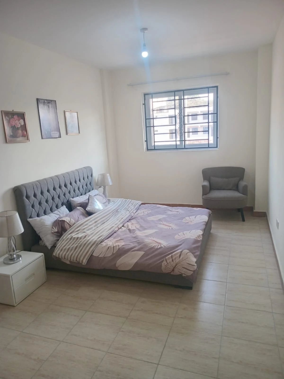 Bedroom in the Ngong Road apartment with a grey tufted bed, armchair and barred window.