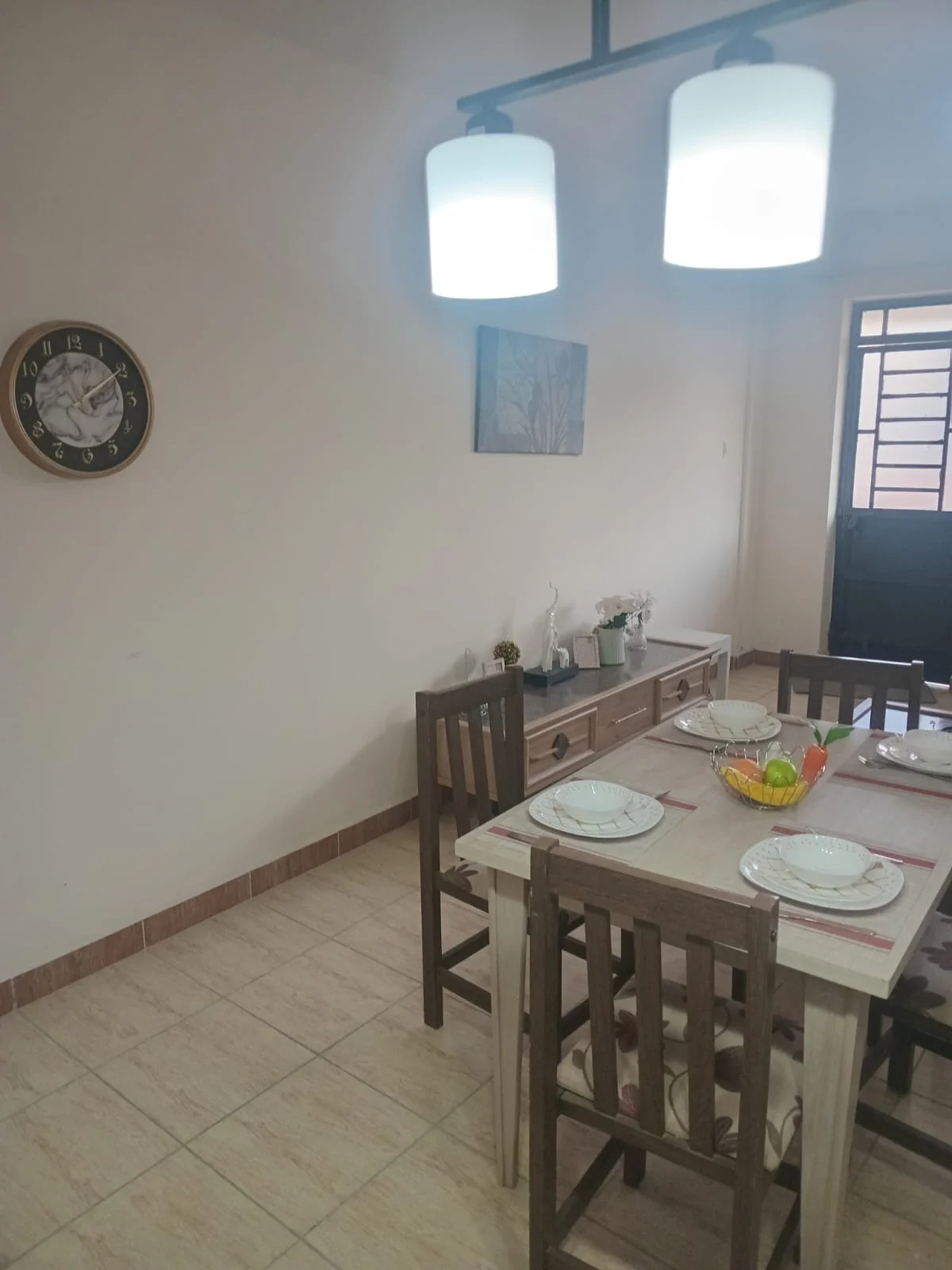 Ngong Road apartment dining area with a set table, wooden chairs and pendant lights.