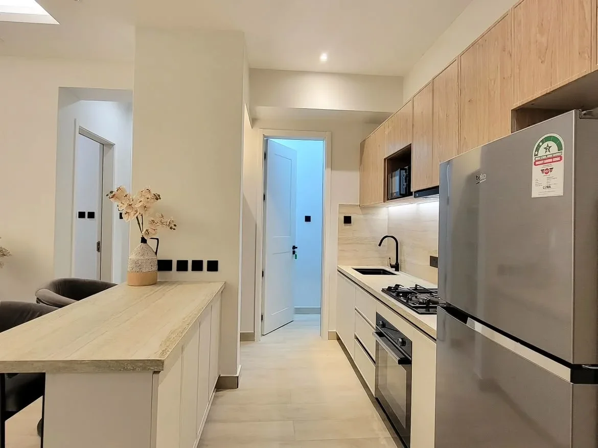 Ngong Road apartment kitchen with wood-look cabinets, breakfast bar, refrigerator, and built-in oven.