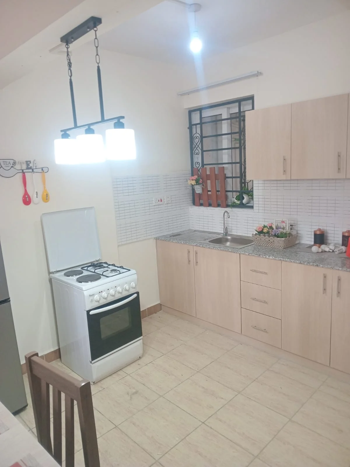 Ngong Road apartment kitchen with pale cabinets, a freestanding cooker, sink and pendant lighting.