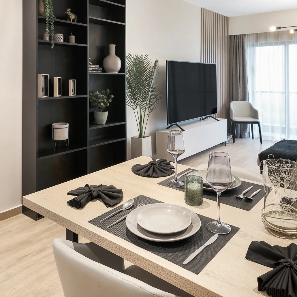 South C apartment dining table set with plates and glassware, beside shelving and a television.