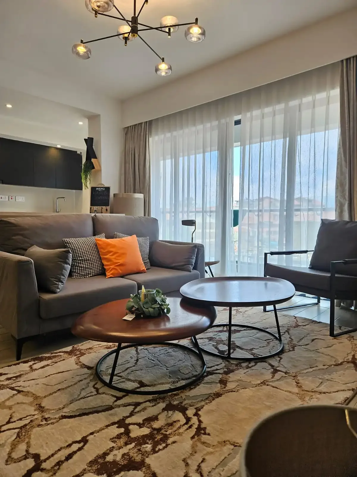 South Park apartment living room with grey seating, round coffee tables and large windows with sheer curtains.