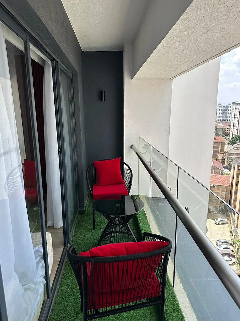 Balcony at South Park Apartments, South C, with red-cushioned chairs, a round table and glass railing.