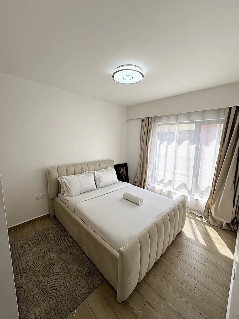 Bedroom at South Park, South C, with an upholstered bed, white bedding and a large curtained window.