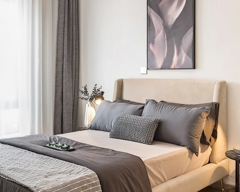 Bedroom at South Park, South C, with a beige upholstered bed, grey pillows and framed abstract artwork.