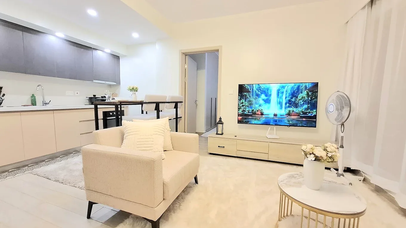 South Park apartment living area with a cream armchair, wall-mounted TV and open kitchen in South C.