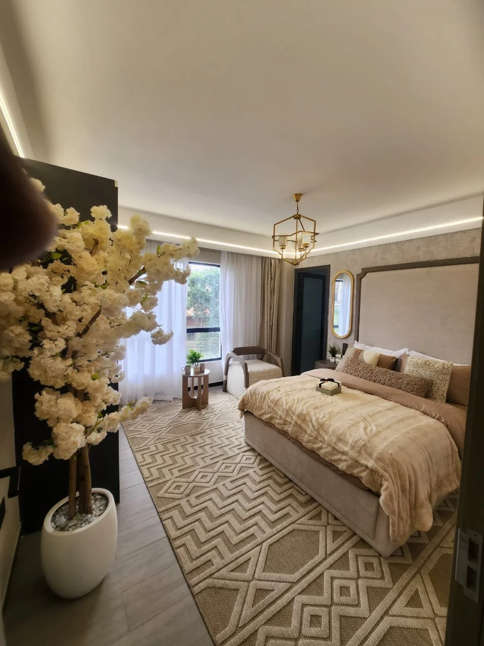 Bedroom at Super Westbury, Westlands, with a beige bed, geometric rug, armchair and curtained window.