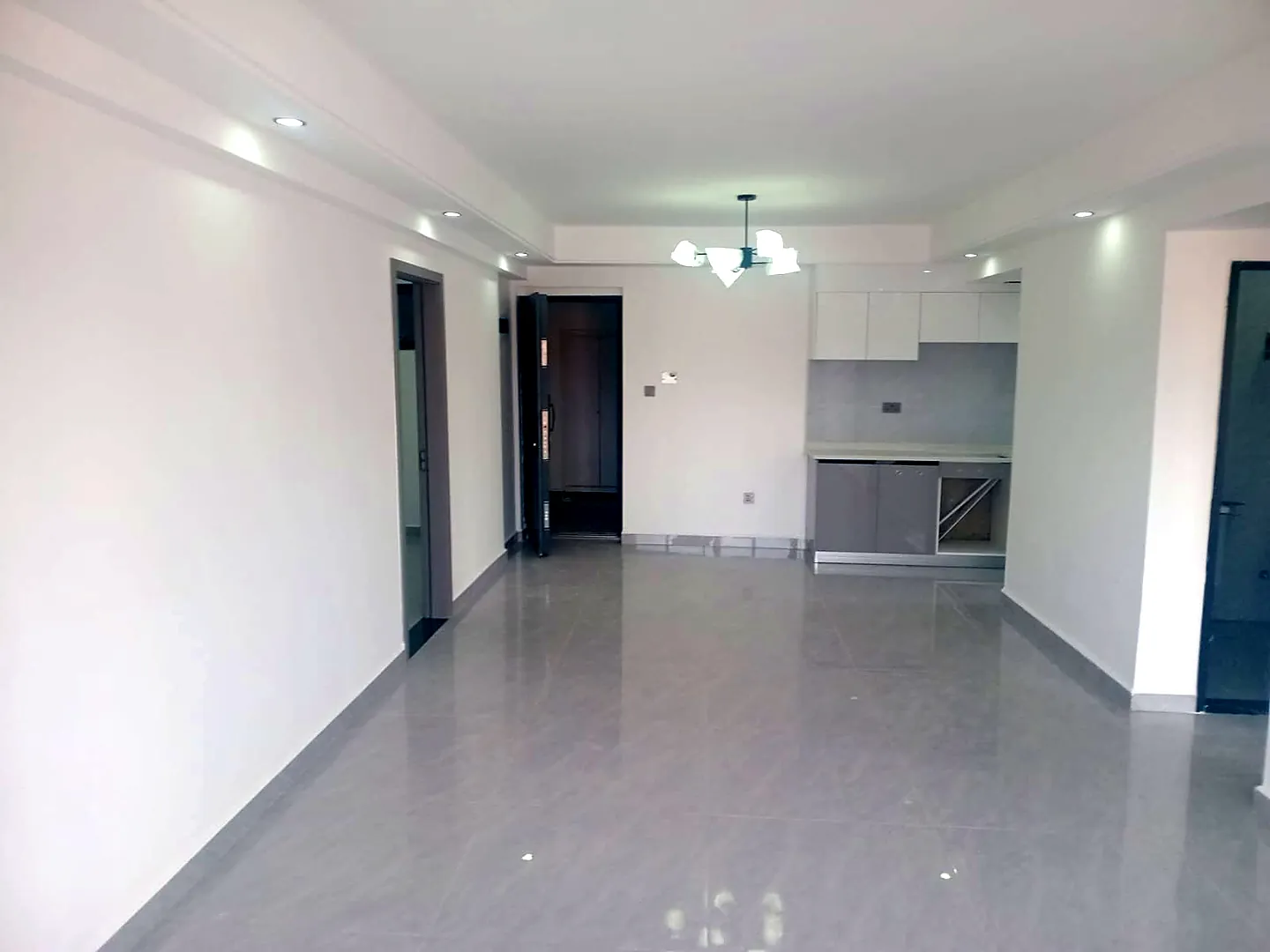 Unfurnished living area at Versailles Garden, Kileleshwa, with grey tiled flooring, ceiling lights and built-in cabinets.