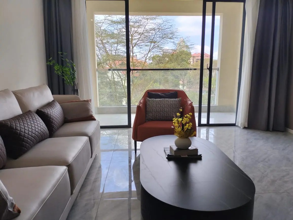 Living room at Versailles Garden, Kileleshwa, with a sofa, armchair, coffee table and sliding glass balcony doors.